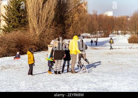 POZNAN, POLAND - Jan 17, 2021: Adults and kids walking with a sled on white snow at a park on a cold winte Stock Photo