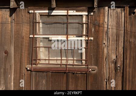 Old rusty bars on old wooden house window, illustrating the concept of an abandoned place or a window closed long ago Stock Photo