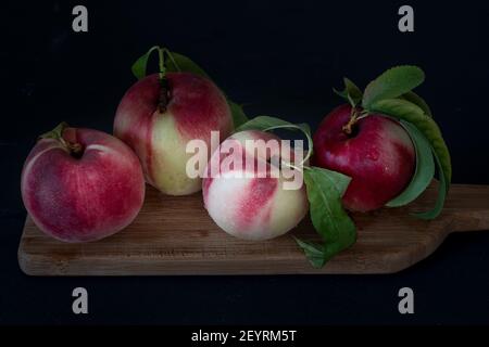 Fresh peaches  with leaves against black background on a wooden board: four whole , viewed form an angle and from close Stock Photo