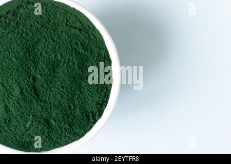 Chlorella powder in a white bowl on a blue background with place for text. Healthy food concept. Horizontal orientation. Stock Photo