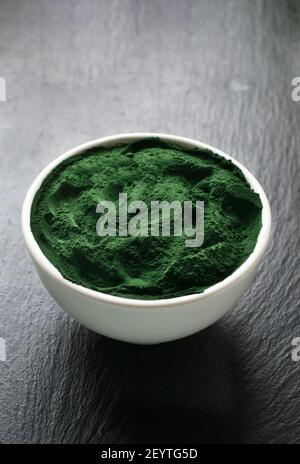 Spirulina powder in a white bowl on a stone background. Healthy food concept. Vertical orientation. Copy space. Stock Photo