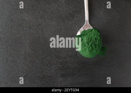 Chlorella powder in a metal spoon on a stone background. Healthy food concept. Horizontal orientation. Top view. Copy space. Stock Photo