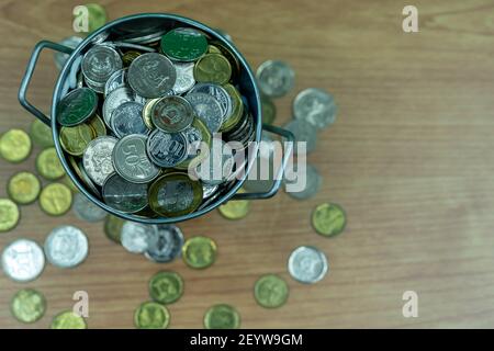 Many coins are in silver buckets on a green background. Money overflow from bucket. Coins overflow from silver bucket Stock Photo