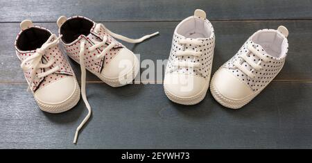 Baby shoes on blue wood floor background. White with pink and blue dots small size sneakers, canvas booties Twins boy and girl concept, banner Stock Photo
