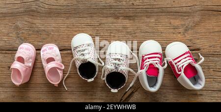 Baby girl first steps. Three pairs of newborn shoes variety on wood floor background, top view. Kids footwear, booties and soft infant shoes in a row. Stock Photo