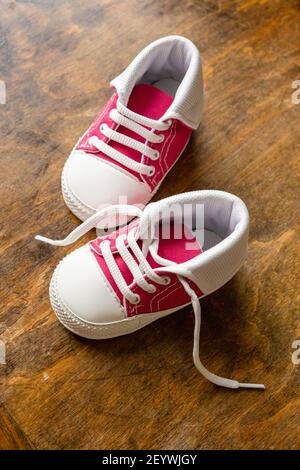 Baby sport shoes on wooden floor. Kid small size pink red sneakers, canvas booties closeup view. Vertical Stock Photo