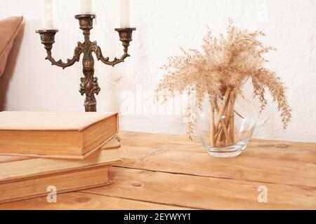 Beige interior, brown books, pampas in a glass vase, candlestick. A wooden bedside table. copy space mocup Stock Photo