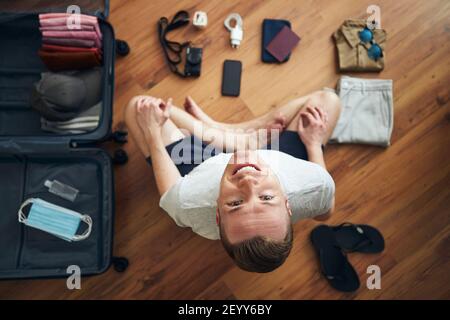 Happy traveler is preparing for travel in new normal. Man packing suitcase with passport, smart phone, clothing and face masks and hand sanitizer for Stock Photo