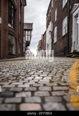 Old historic cobbled high street with selective focus on cobble stones with yellow line painted winding road leading up through town centre building Stock Photo