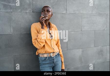 Afro senior woman smoking cigarette while standing against urban wall Stock Photo