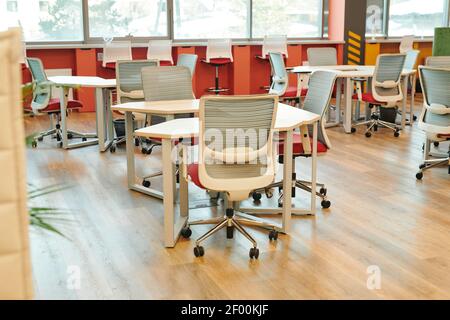 Interior of contemporary large open space office with many chairs by tables and along windowsills with no workers or managers around Stock Photo