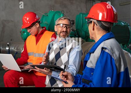 Technical Manager Using Digital Tablet and Talking to Two Power Plant Workers. District Heating Power Plant. Digital Technology Concept. Industry 4.0 Stock Photo