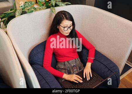 Confident young female office manager or designer in smart casualwear looking at laptop display while preparing presentation or networking Stock Photo