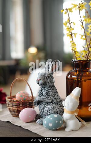 Grey and white toy rabbits, basket with painted Easter eggs and vase with yellow flowers standing on wooden table in front of camera Stock Photo