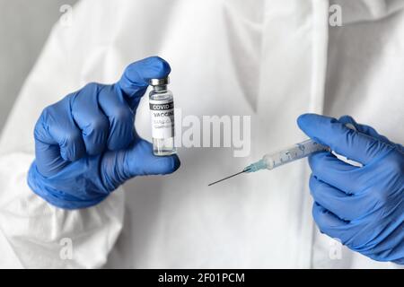 COVID-19 coronavirus vaccine in doctor hands, nurse in white PPE suit holds vaccine bottles and syringe for injection. Concept of vaccination, medical