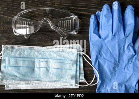 COVID-19 coronavirus medical kit, top view of surgical mask, protective glasses and gloves. Flat lay composition of personal equipment (PPE). Concept Stock Photo