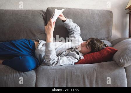 Young man stretching comfortably on couch and reading a book. Man relaxing at home Stock Photo