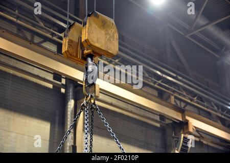 Lifting mechanism in the workshop at the plant. Crane hook and chains. Stock Photo