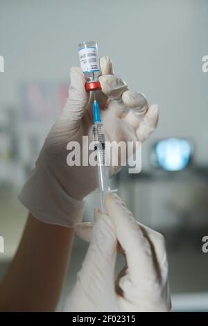 Gloved hands of clinician or nurse holding syringe and small bottle with new vaccine while preparing injection for patient with covid19 Stock Photo