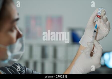 Gloved hands of young female clinician or nurse in protective mask preparing injection for patient in medical office of modern clinics Stock Photo