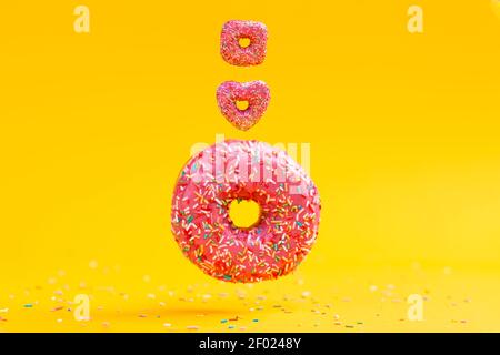 Three doughnuts of different shapes and sizes, with pink icing. Yellow background. Copy space. Stock Photo