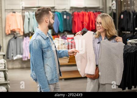 Young woman choosing vest for herself together with her boyfriend who giving her an advice in the store Stock Photo