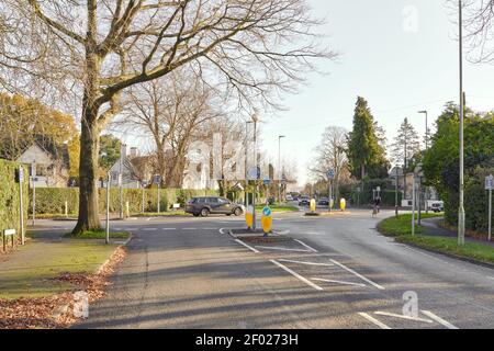 Double mini-roundabout on a city residential road, with trees a street lights, with a lot of road and directional signs. Shows a cyclist and car. Stock Photo