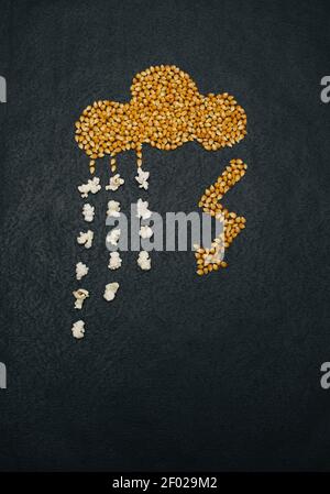 Cloud and lightning made of corn grain on a black textured background, rain drops turning from corn to popcorn. Creative top view contrast concept. Stock Photo