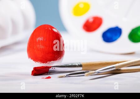 Painting Easter eggs, Preparation for spring holiday, Red egg with palette of colors on blue background, Paint Brushs, Copyspace Stock Photo