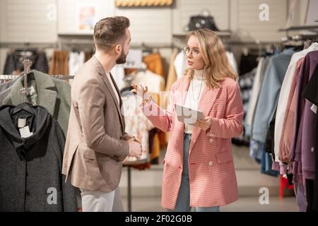 Young stylist using digital tablet while talking to the customer in the clothing shop in the mall Stock Photo