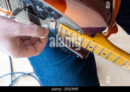 Closeup vertical view looking down on a man at home playing a Fender Telecaster Modern Player electric guitar with a plastic pick Stock Photo
