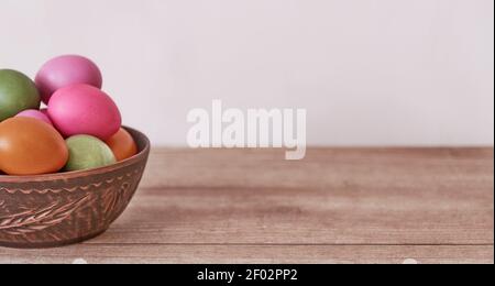 Colored chicken eggs painted with natural food dyes in a clay plate on a wooden table. Banner. Easter holiday concept Stock Photo