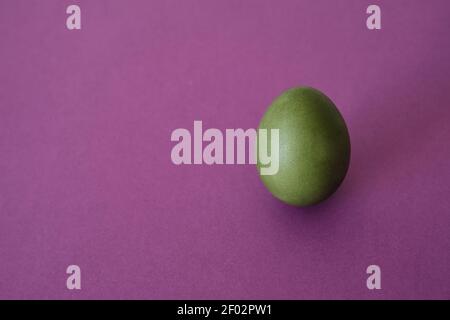 Painted green egg on a violet background. Abstract composition. Top view. Easter holiday concept. Stock Photo