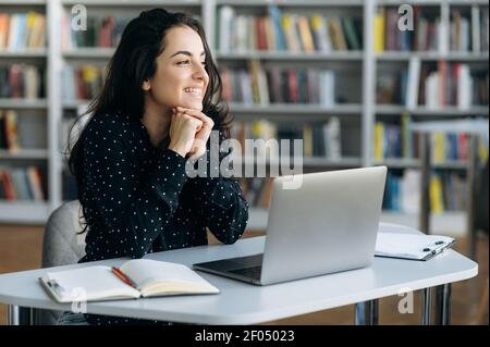 Happy young woman at the workplace modern office, using laptop. Caucasian female freelancer or student thinking about weekends while working or studying Stock Photo