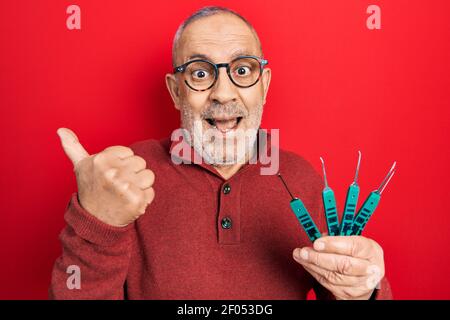 Handsome mature man holding picklock to unlock security door pointing thumb up to the side smiling happy with open mouth Stock Photo