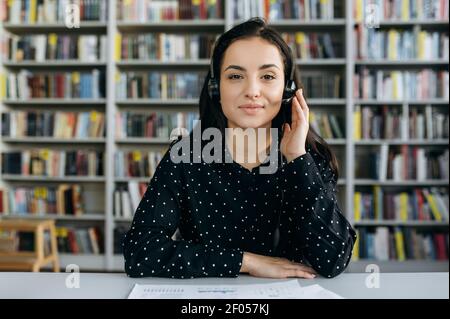Webcam portrait of successful business woman. Confident female manager on video meeting, looking directly at the camera. Caucasian lady sitting at the desk, wearing headset, communicate with Stock Photo