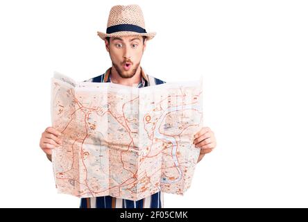 Young handsome caucasian man wearing summer hat holding city map scared and amazed with open mouth for surprise, disbelief face Stock Photo