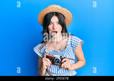 Young beautiful caucasian girl holding vintage camera in shock face, looking skeptical and sarcastic, surprised with open mouth Stock Photo