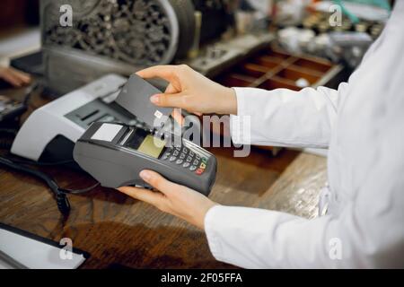 Cashless payment at pharmacy. Cropped close up shot of hands of female unrecognizable pharmacist in lab coat, working at old pharmacy and swiping Stock Photo