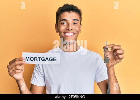 Young handsome african american man holding paper with mortgage word and house keys smiling with a happy and cool smile on face. showing teeth. Stock Photo