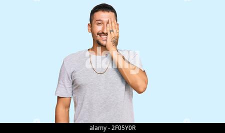 Handsome man with tattoos wearing 90s style covering one eye with hand, confident smile on face and surprise emotion. Stock Photo