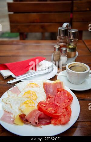 Fried eggs,bacon,tomatoes,ham and coffee in a cup with cutlery and napkins.Salt and pepper in the background. Stock Photo