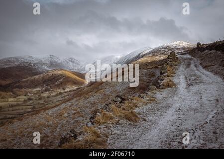 Snow and ice covered Garburn track as it ascends from Troutbeck towards Kentmere with Troutbeck Tongue and the Ill Bell ridge in the distance Stock Photo
