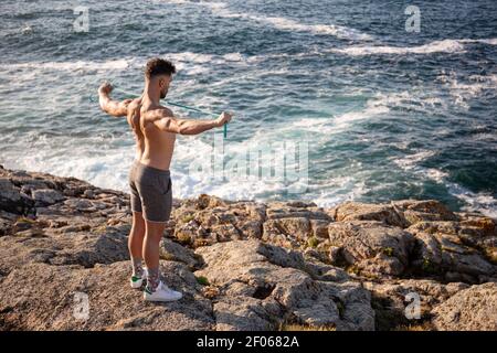 Back view of unrecognizable female traveler standing on wooden pier near vessels and admiring picturesque view of small Llanca municipality with buildings and cloudy sky reflected in calm water in sunny day in Spain Stock Photo