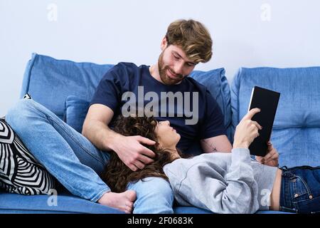From below young Woman in casual clothe lying on sofa and reading book putting head on knees of boyfriend Stock Photo