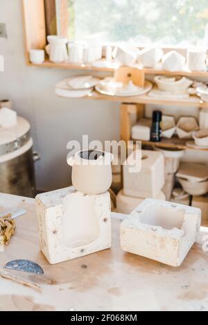 Light studio with ceramic pots on surface near shelf with handmade clayware Stock Photo