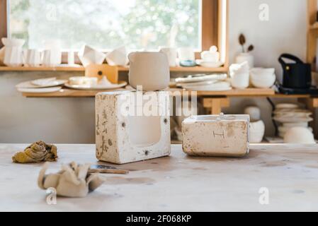 Light studio with ceramic pots on surface near shelf with handmade clayware Stock Photo