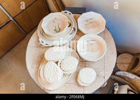 From above of assorted dishware made of clay placed on round table in pottery workshop Stock Photo