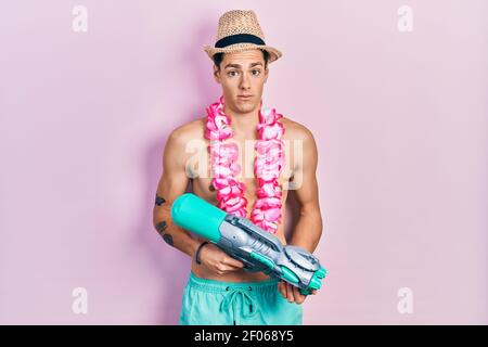 Young hispanic man wearing swimsuit and watergun clueless and confused expression. doubt concept. Stock Photo