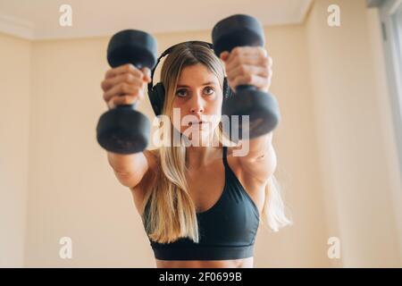 Determined female in sportswear with headphones listening to music while doing lunges exercise with weight at home Stock Photo